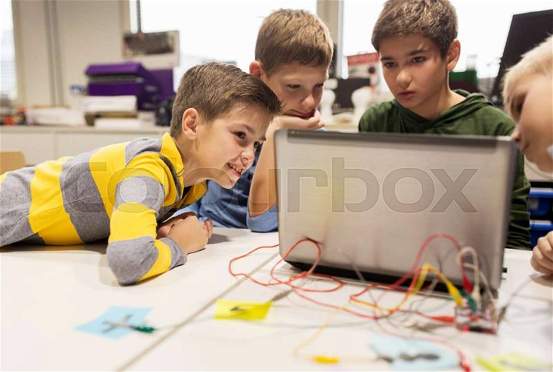 Education, children, technology, science and people concept - group of happy kids with laptop computer playing with invention kit at robotics school lesson, stock photo