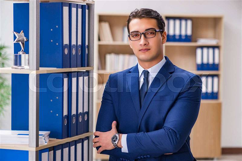 Young man standing next to the shelf with folders, stock photo