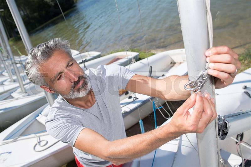 Attractive middle-aged man preparing sport sailboat, stock photo