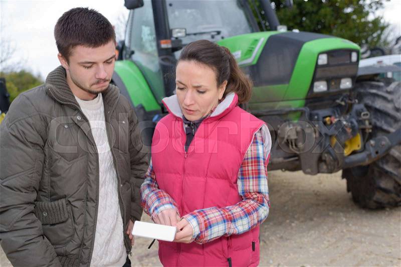Young cheerful farming couple checking their tractor before the harvest, stock photo