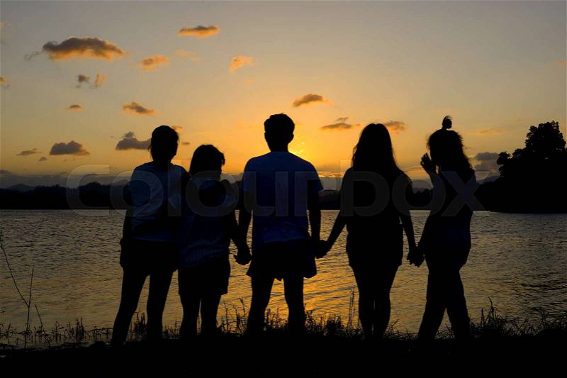 Silhouette group of friends standing hand in hand in sunset, stock photo