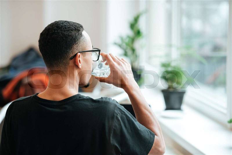 Back view of a young african man drinking water out of glass during coffee break at cafe, stock photo