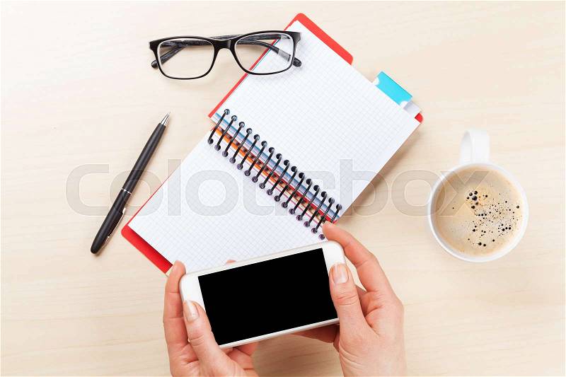Woman holding smartphone above business desk. Top view with copy space, stock photo