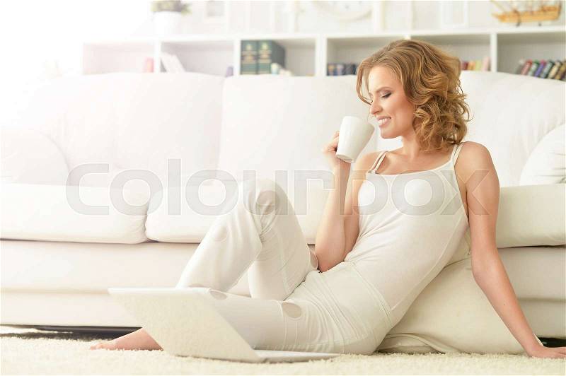 Young beautiful woman using laptop and drinking tea on the floor at home, stock photo
