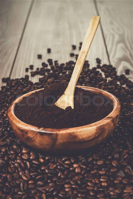 Coffee beans and wooden bowl full of ground coffee on the table background, stock photo