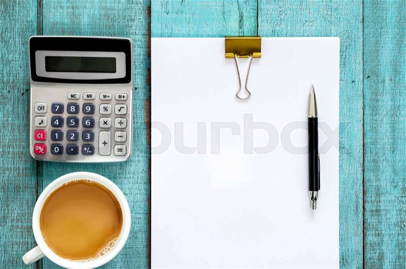 Blue wooden desk table with paper ream, pen, calculator and cup of coffee. Top view with copy space, flat lay, stock photo