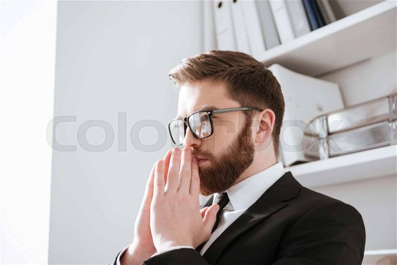 Photo of attractive young bearded businessman sitting in office while looking aside, stock photo