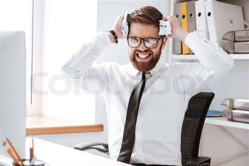 Picture of confused businessman wearing glasses dressed in white shirt sitting in office and holding paper, stock photo