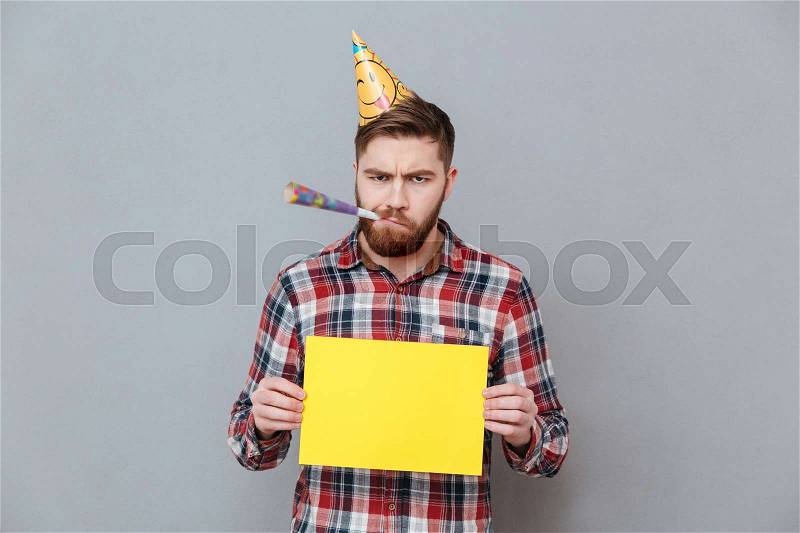 Photo of confused sad young bearded birthday man holding copyspace board standing over grey background, stock photo