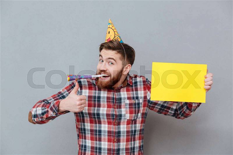 Photo of cheerful young bearded birthday man holding copyspace board make thumbs up gesture standing over grey background, stock photo