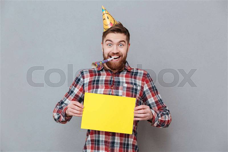 Picture of happy young bearded birthday man holding copyspace board standing over grey background, stock photo