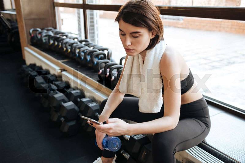 Fitness woman with towel using mobile phone in gym, stock photo