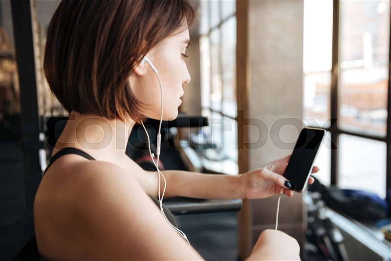 Fitness woman with earphones listening to music from mobile phone, stock photo