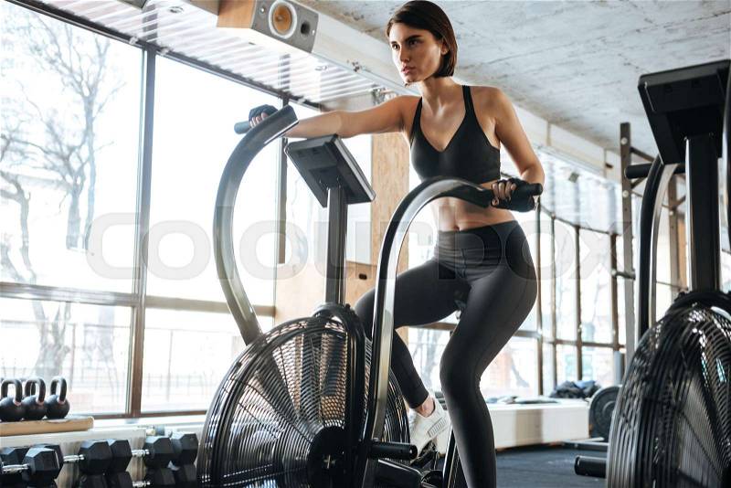 Woman athlete sitting and training on bike in gym, stock photo