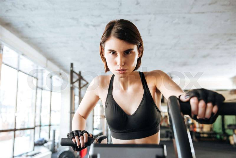 Beautiful young sportswoman training on stationary bike in gym, stock photo