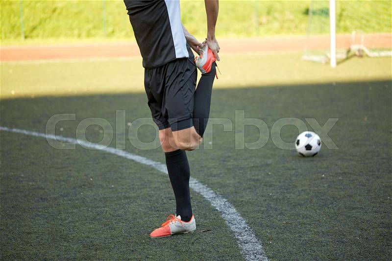 Sport, football training and people - soccer player stretching leg on field, stock photo