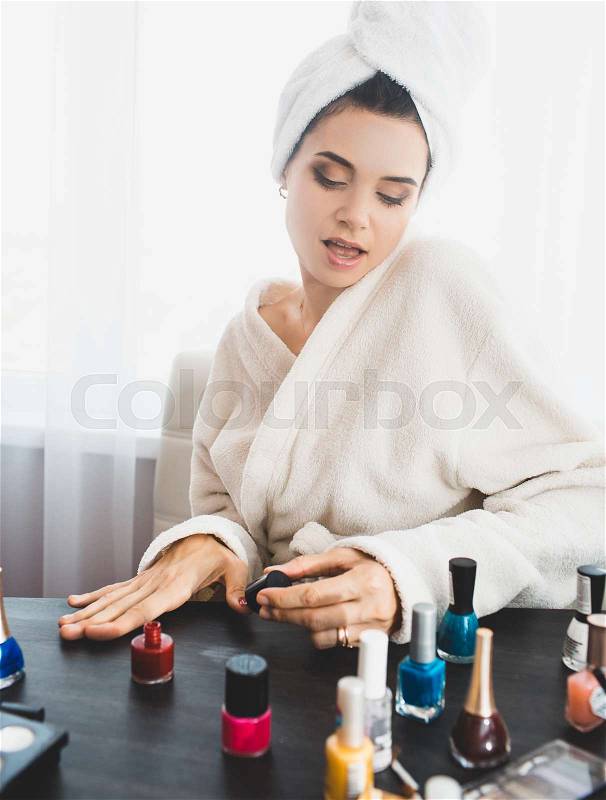 Beautiful woman with towel on her head making manicure, stock photo
