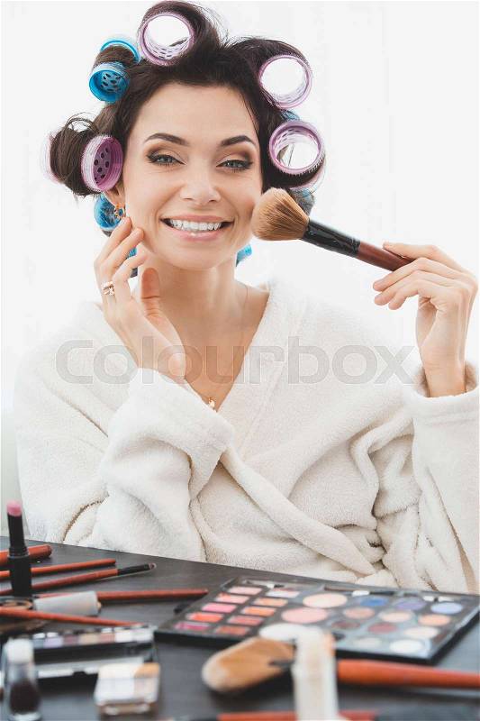 Beautiful woman with curler on her head doing make up, stock photo