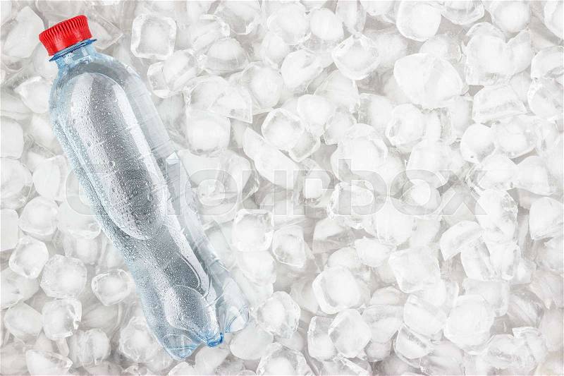 Plastic water bottle with red cap is cooling in the ice, stock photo