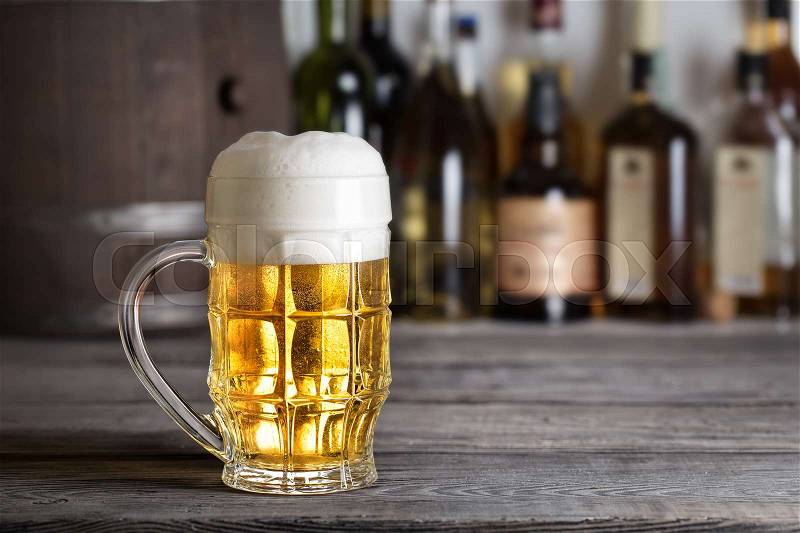 Large glass of light beer with foam on bar counter against background of drums, stock photo