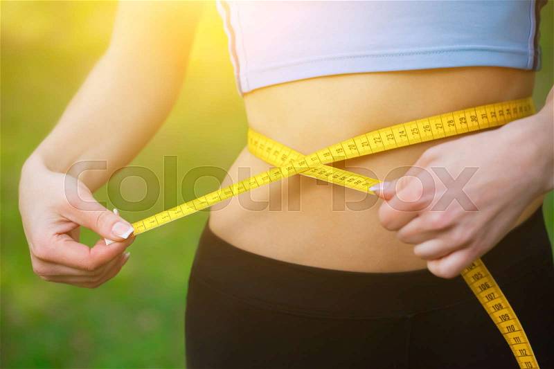 Sport girl measuring waist with yellow measuring tape. Reducing excess weight. Healthy lifestyle, stock photo