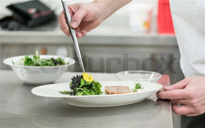 Chef cook finishing salad and pastry dish with pincers and flowers, stock photo