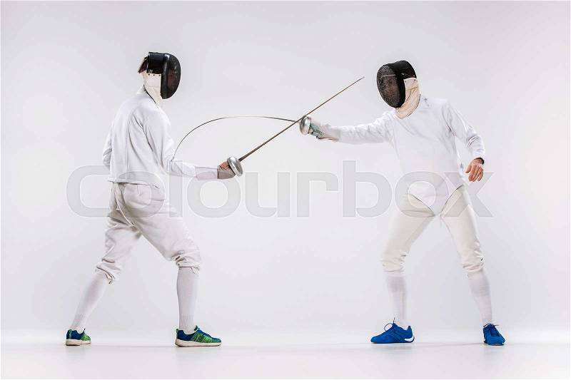 The two men wearing fencing suit practicing with sword against gray studio background, stock photo
