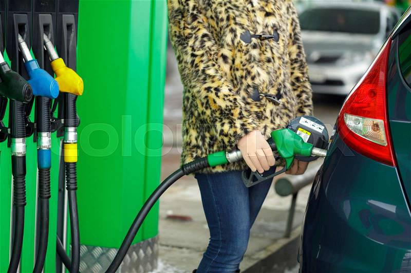 Woman fills petrol into her car at a gas station in winter closeup, stock photo