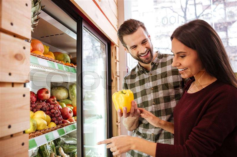 Cheerful young couple choosing and buying vegetables in grocery shop, stock photo