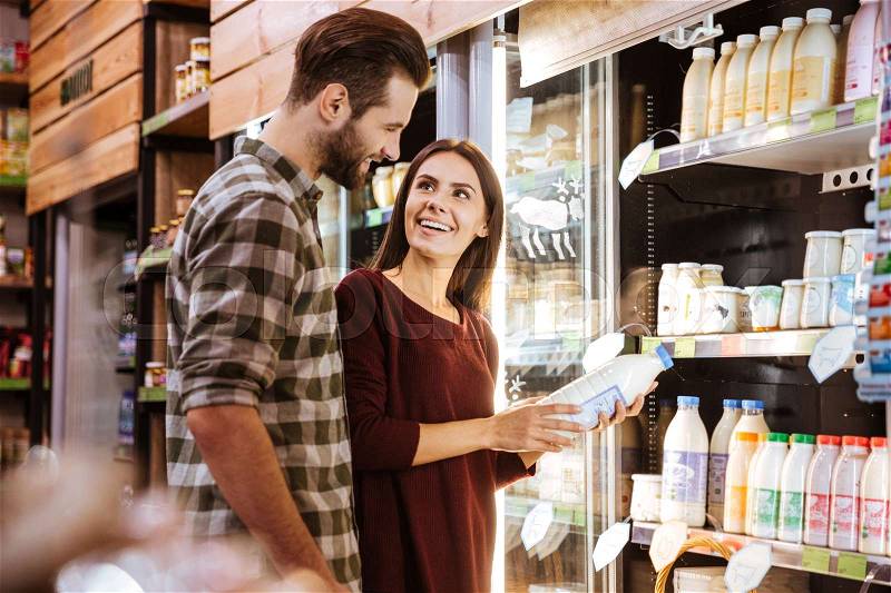 Cheerful young couple talking and buying milk at grocery shop, stock photo
