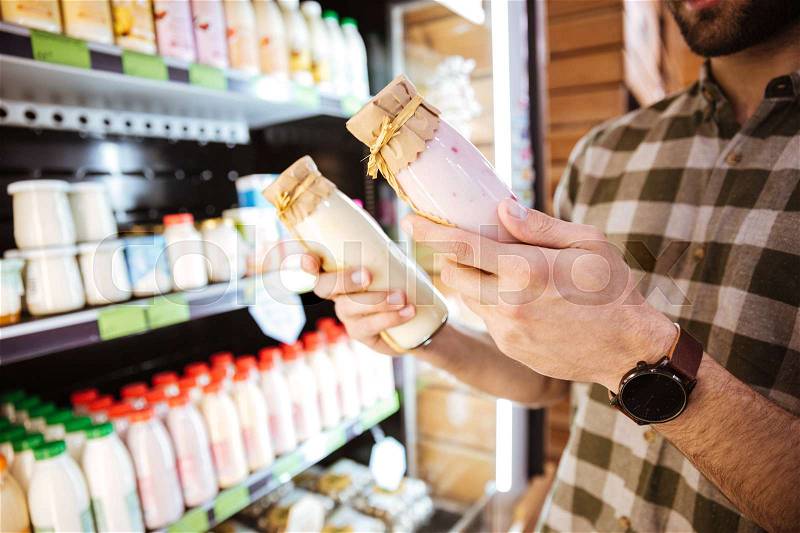 Closeup of man standing and buying yoghurt in bottles at grocery shop, stock photo