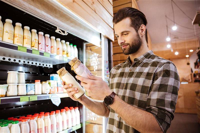 Smiling bearded young man choosing yoghurt in grocery shop, stock photo