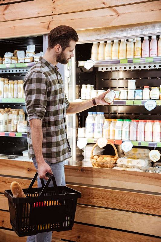 Attractive young man choosing and buying food at grocery shop, stock photo