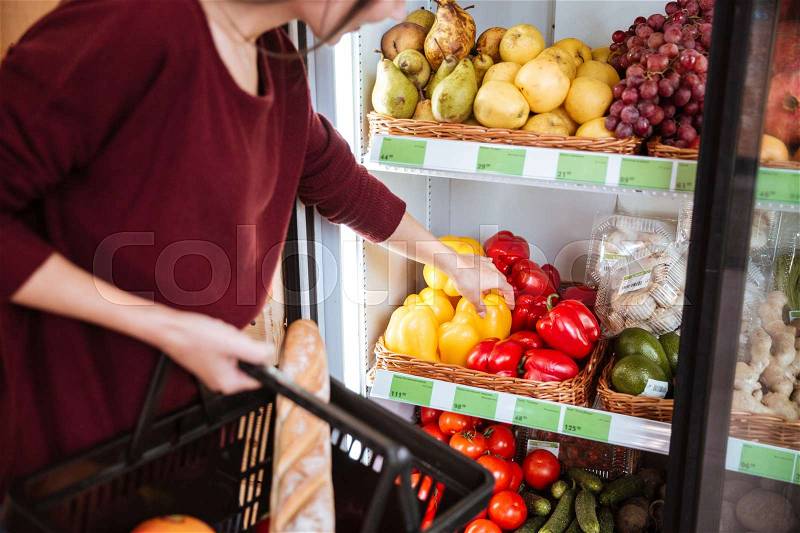 Woman with basket choosing and buying bell pepper in supermarket, stock photo