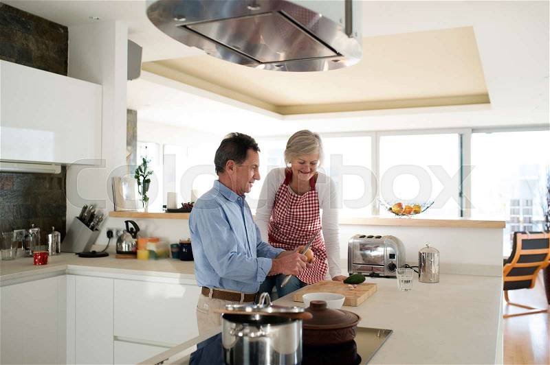 Senior couple in the kitchen cooking together, man cutting onion talking to his wife, stock photo