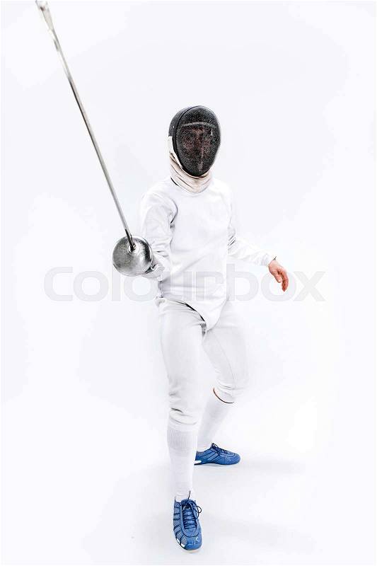 Man wearing fencing suit practicing with sword against gray studio background, stock photo