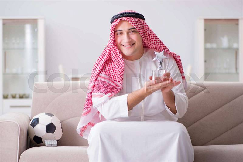 Young arab man watching football sitting on sofa, stock photo