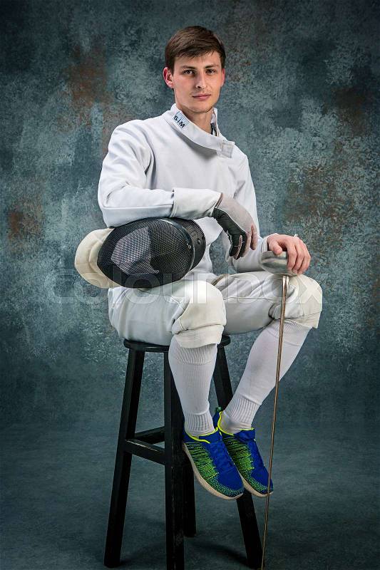 The man wearing fencing suit posing with sword against gray studio background, stock photo