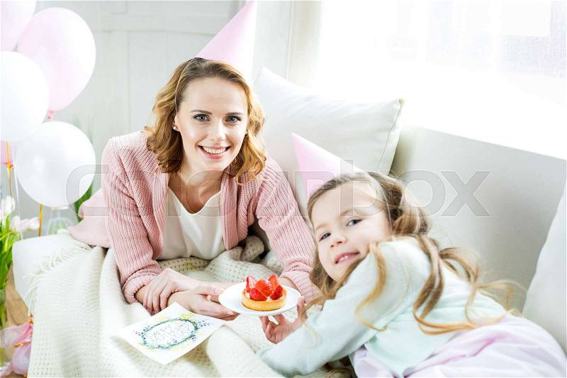 Happy mother and daughter holding tasty strawberry cake and smiling at camera, stock photo