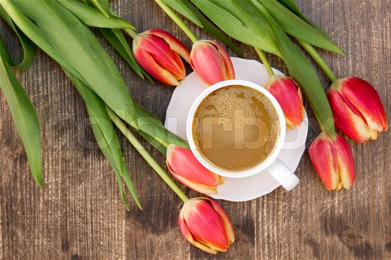 Bunch of red tulips and white cup of coffee on the brown wooden table, stock photo