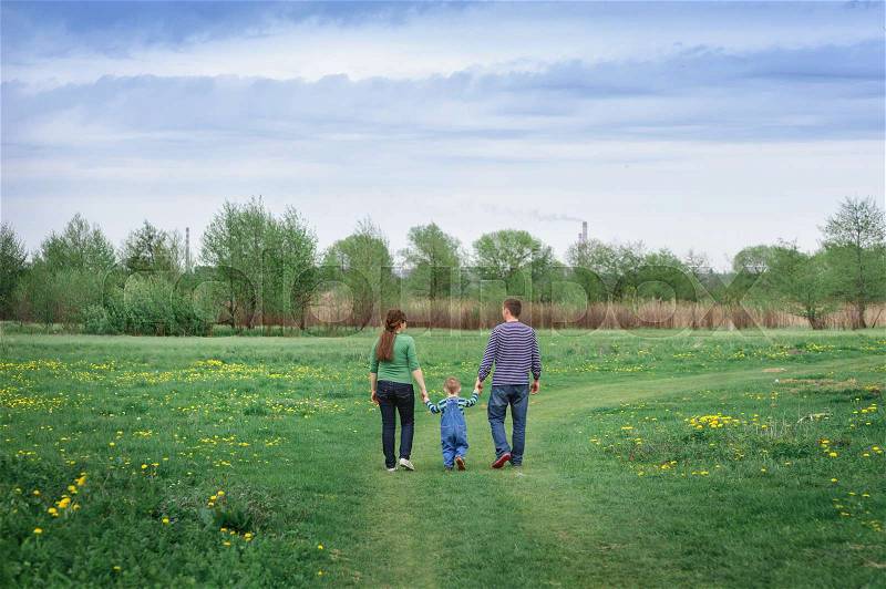 Young family and young son walk on a spring meadow, stock photo