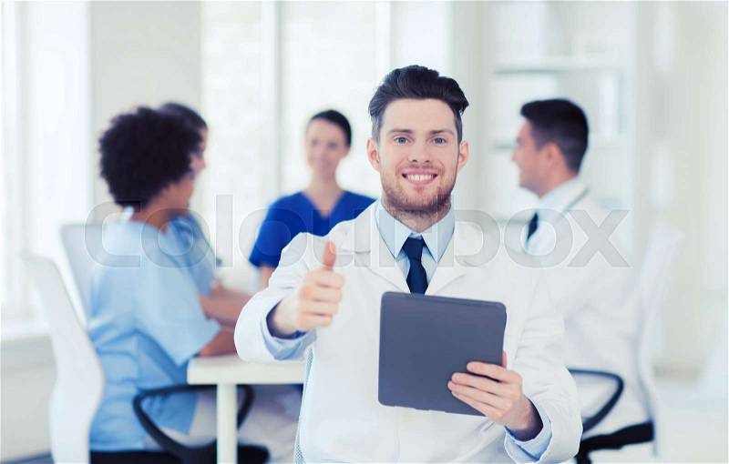 Clinic, profession, people and medicine concept - happy male doctor with tablet pc computer over group of medics meeting at hospital showing thumbs up gesture, stock photo