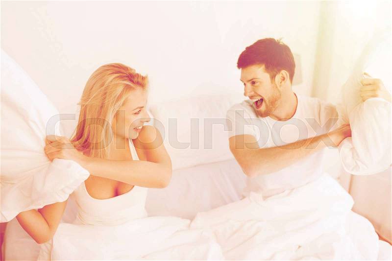 People, family, fun, bedtime and fun concept - happy couple having pillow fight in bed at home, stock photo