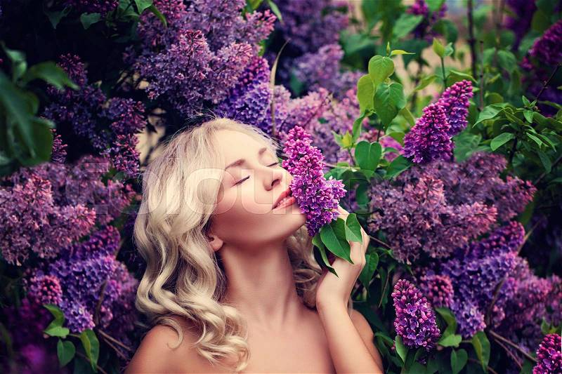 Beautiful Woman Enjoying the Smell of Lilac. Cute Model and Flowers. Aromatherapy and Spring Concept, stock photo