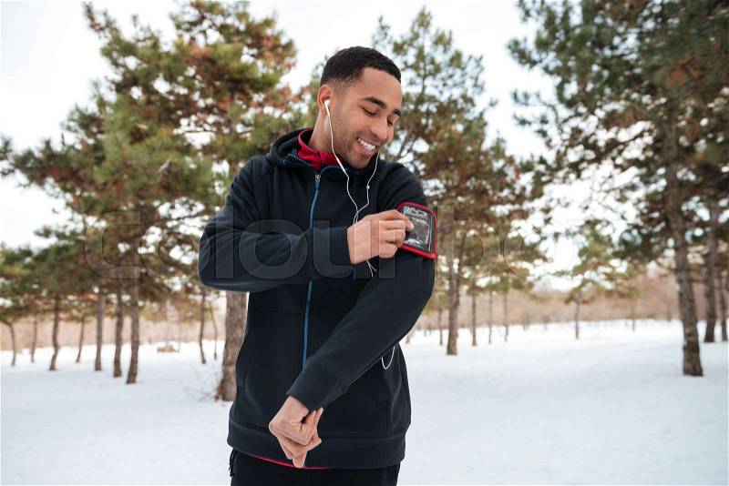 Young sportsman outside in winter park listening to music on smartphone, stock photo