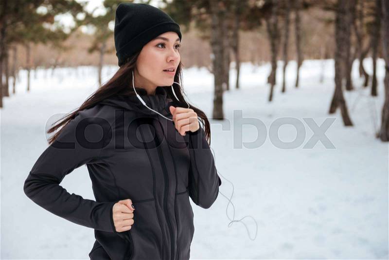 Close up portrait of a woman wearing sportswear running on snow with trees in background, stock photo