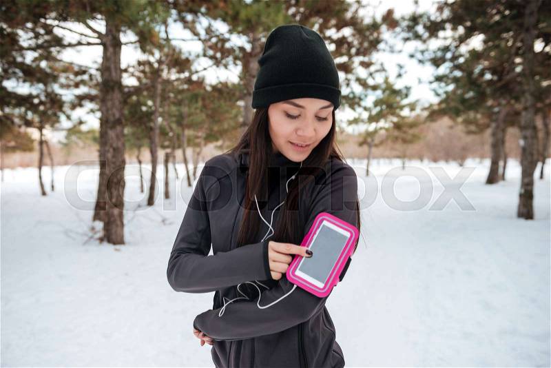 Portrait of a lovely young fitness woman with armband and earphones outdoors, stock photo