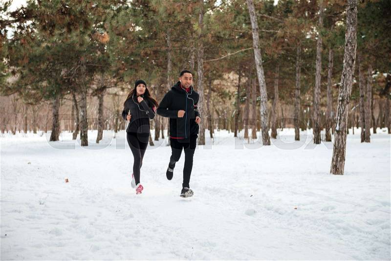 Healthy young couple jogging outside on snow in forest, stock photo