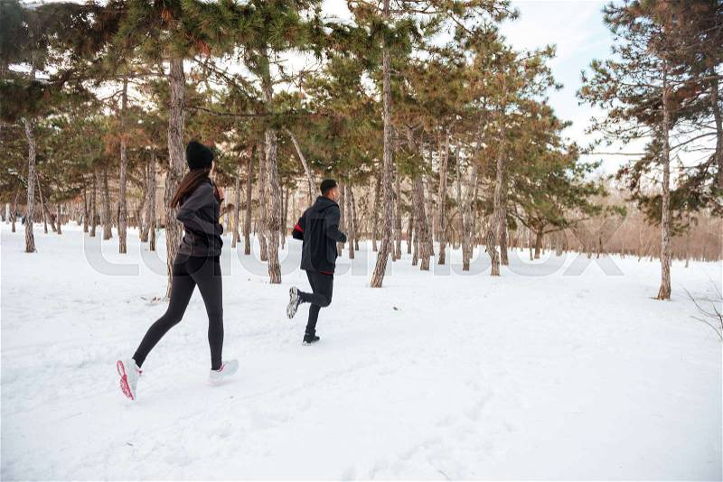 View of a young fitness couple running in the forest in winter, stock photo