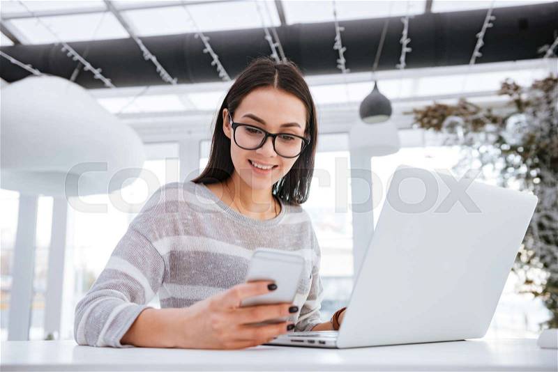 Photo of happy young woman sitting in cafe at cold winter day and chatting by phone, stock photo